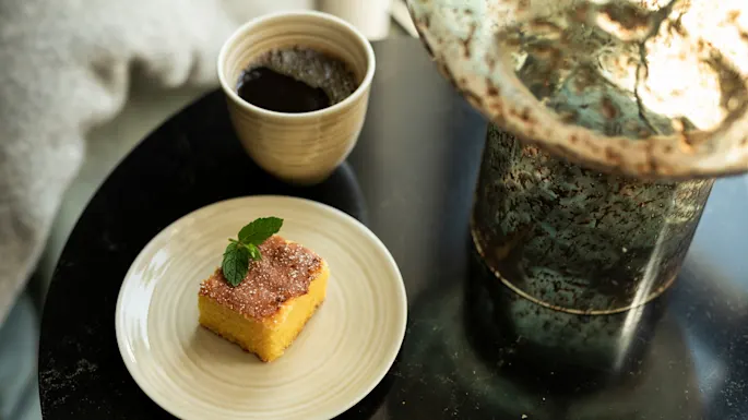 A delicious slice of cake with a mint garnish and a cup of coffee on a dark table, suggesting a pleasant break.