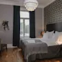 Mukava hotellihuone sisältää siististi pedatun sängyn valkoisin vuodevaattein kuvioitua seinää vasten. Kirjoituspöytä ja tuoli ovat lähellä pehmeässä valaistuksessa. Ikkunasta on näkymä ulos.