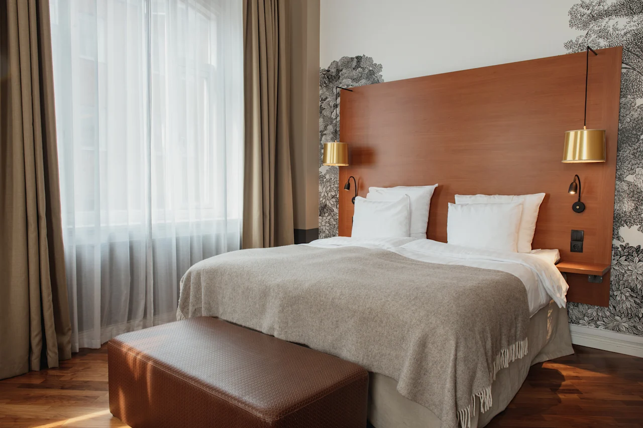Et koselig hotellrom med en stor seng, sengegavl i tre og myk belysning, klart for et komfortabelt opphold.