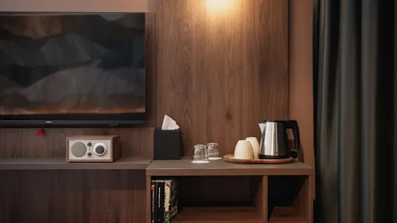 Et velutstyrt hotellrom med en mediekonsoll og en praktisk drikkestasjon, klart for gjestens komfort.