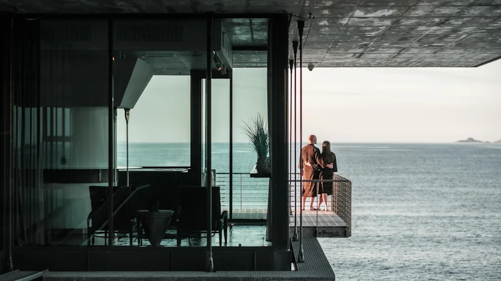 Two people on a balcony at Farris Bad, looking out at the vast, calm sea.