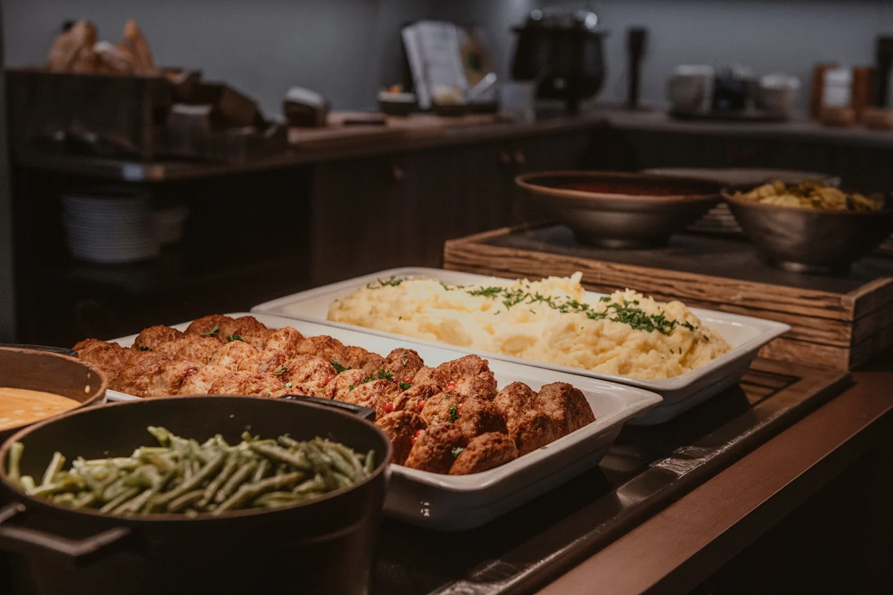 En varm buffé med köttbullar, potatismos och gröna bönor, redo att serveras i en mysig matsal.