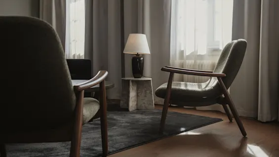 Ett mysigt hotellrum med två fåtöljer, en lampa och solljus genom fönstret, vilket skapar en varm atmosfär.