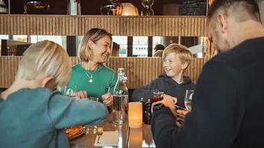 En smilende familie med to unge drenge der nyder en middag sammen ved et moderne restaurantbord.