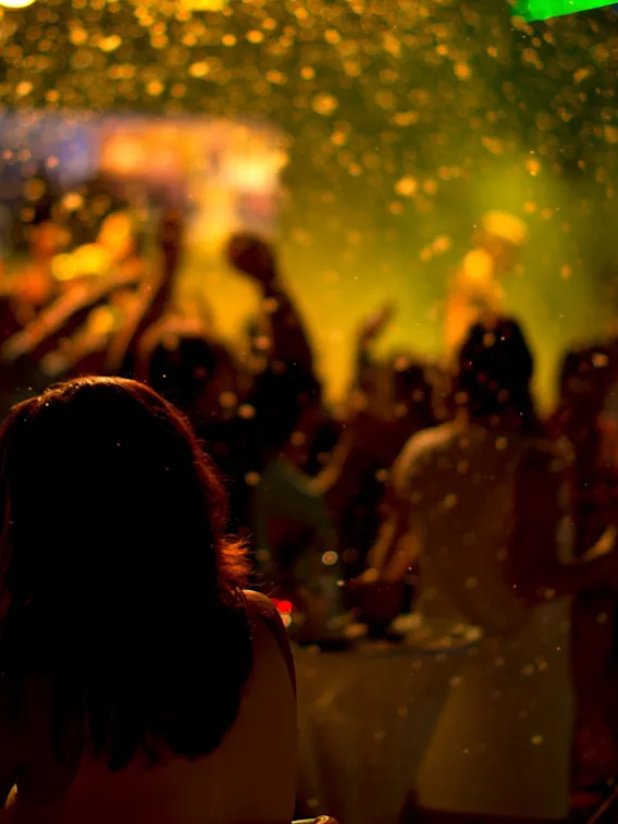 Silhouettes of people dancing at a lively party under warm lighting with golden confetti falling from above.