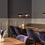 Et innbydende spiseområde med myke lilla stoler, trebord og varm stemningsbelysning fra hengende armaturer.