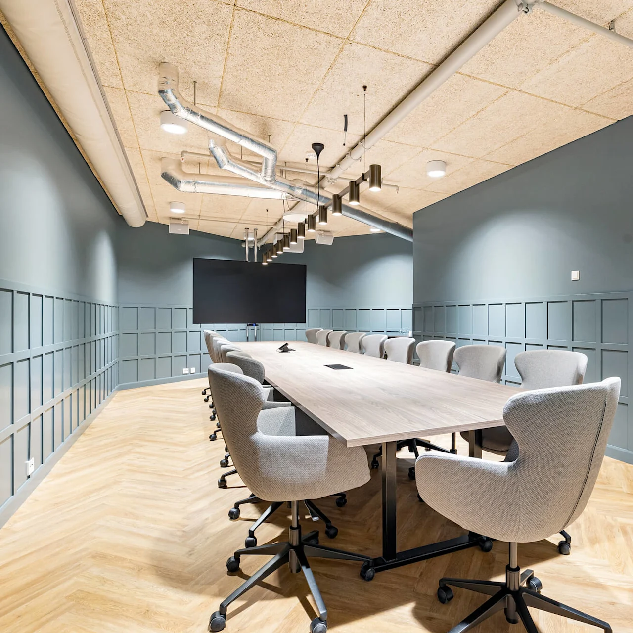A conference room with a long table and chairs, a screen on the wall, under exposed ceilings.