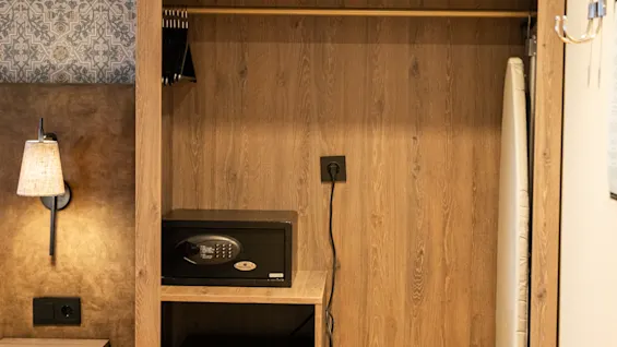 Ett träskåp med vikta handdukar och ett strykjärn på hyllan, ett kassaskåp och minibar nedanför, i ett mysigt, varmt belyst rum med mönstrad tapet.