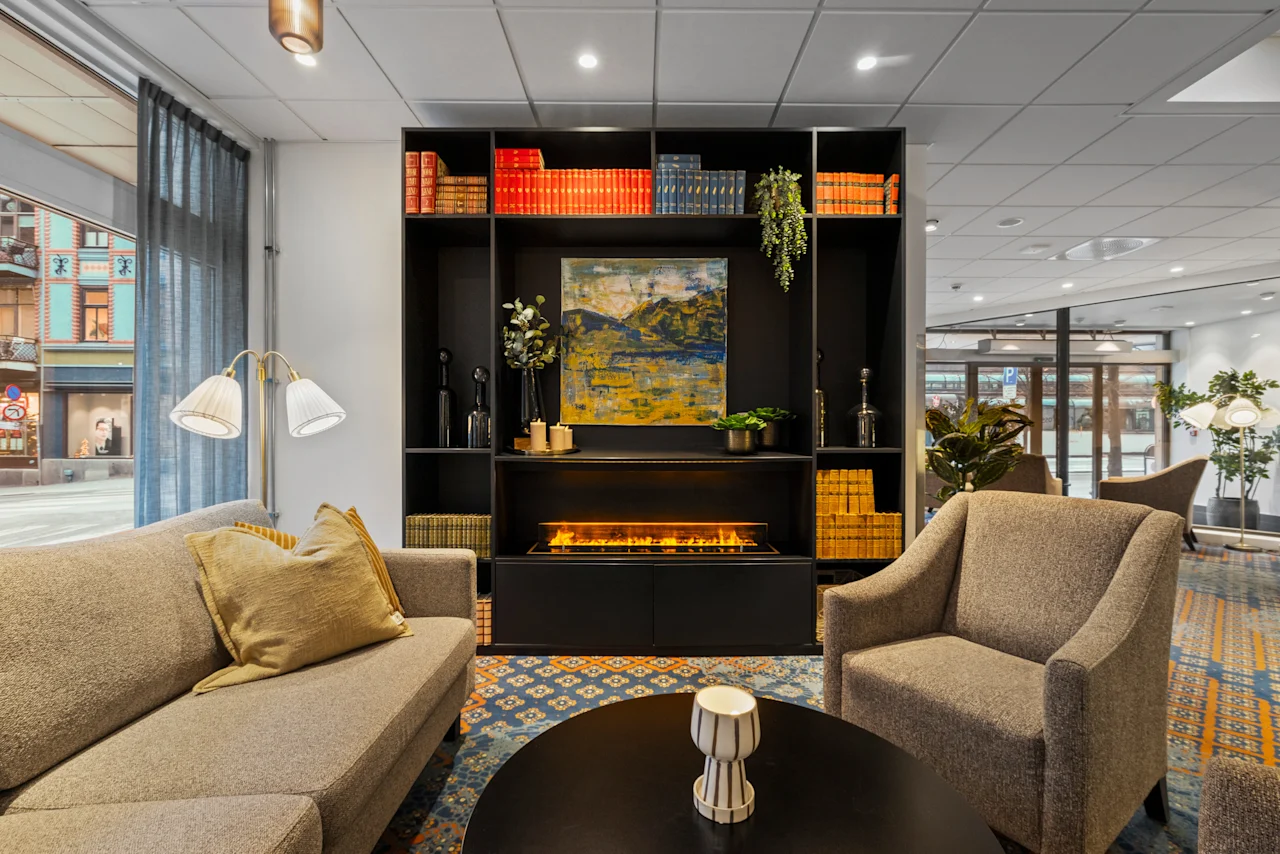 En mysig hotellounge med en bekväm sittgrupp, ett soffbord och en stilren bokhylla med en varm öppen spis.
