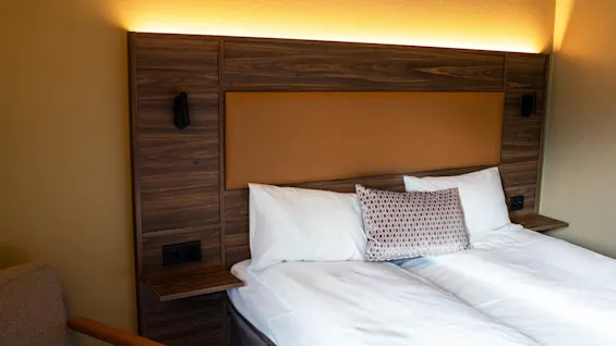 A cozy hotel room featuring a bed with a stylish wooden headboard, warm lighting, and comfortable pillows.