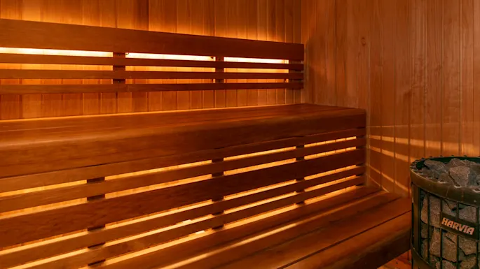 Trekledd badstueinteriør med to-nivå benker langs veggene. Dempet belysning forsterker den varme, koselige atmosfæren. En metallovn med steiner i hjørnet.
