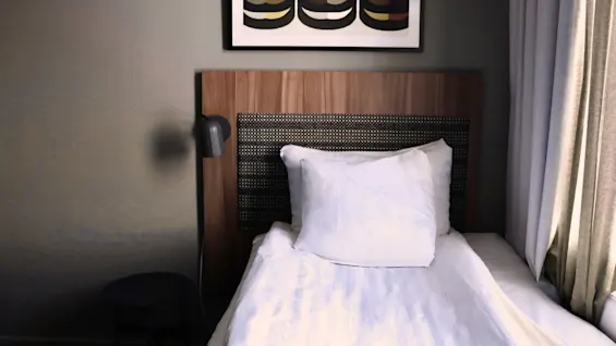 En pænt redt enkeltseng på et moderne hotelværelse med sengegavl i træ, væglampe og abstrakt kunst.
