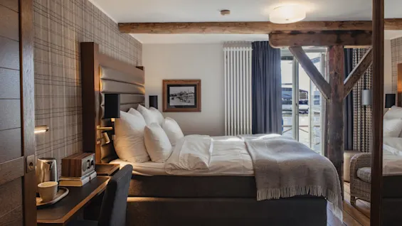 Et hyggeligt hotelværelse med en komfortabel seng, et lille skrivebord og udsigt til udendørs gennem et stort vindue.