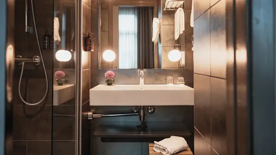 A modern and well-lit hotel bathroom featuring a sink, mirror, and shower, with fresh towels and a touch of decor.