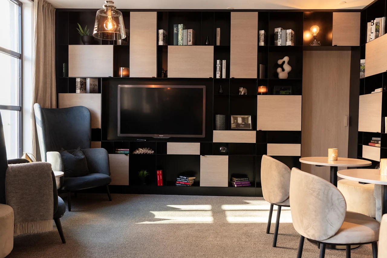 En indbydende hotellounge med en stor skærm, integrerede hylder fyldt med bøger og indretning samt komfortable siddepladser.