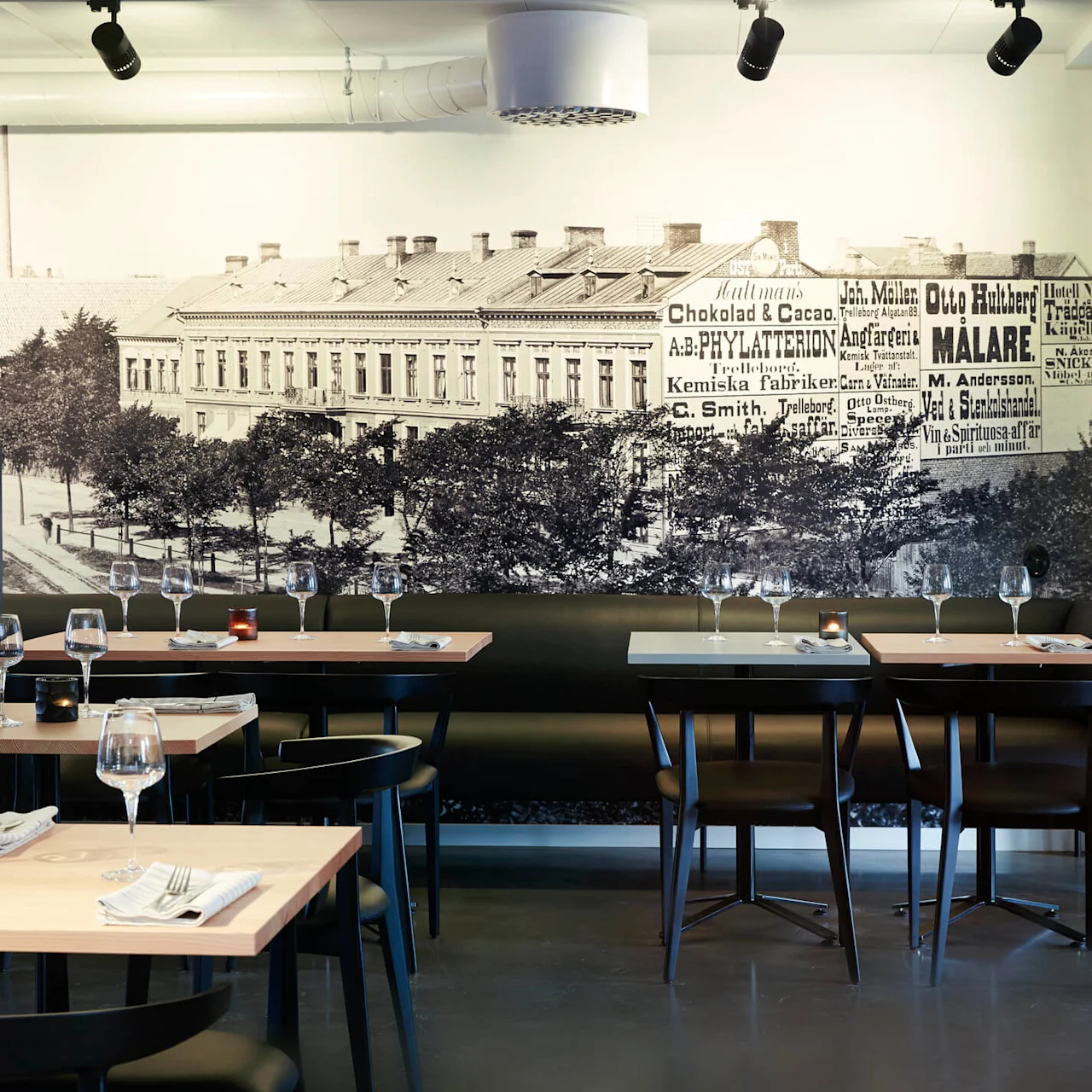 A sophisticated restaurant interior with tables set for dining, a large historic photo mural on the wall, and pendant lighting.