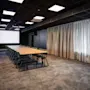 A modern conference room with a long table, chairs, a large projector screen, and sheer curtains, ready for a presentation or meeting.