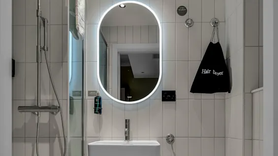 Ett modernt badrum med belyst spegel, dusch, handfat och toalett i minimalistisk stil. Text på väggen lyder "Hair Dryer".