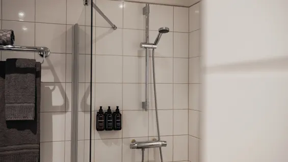 Ett rent och inbjudande duschutrymme med vita kaklade väggar, en glasvägg, ett duschhuvud, fräscha handdukar och praktiska toalettartiklar.