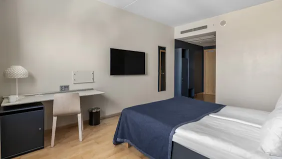 Et moderne hotelværelse med komfortabel seng, funktionelt skrivebordsområde og vægmonteret TV, til afslapning og arbejde.