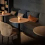Et hyggeligt, dæmpet loungeområde med små borde, komfortable stole og en lang bænk, hvert bord med et flimrende lys.
