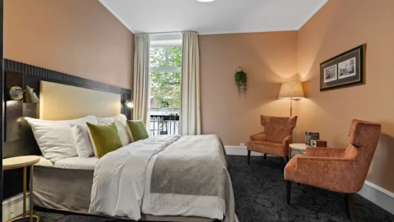 Et koselig hotellrom på Home Hotel Gabelshus med en komfortabel seng, to lenestoler og utsikt over grøntområder.