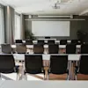 Ett väl upplyst konferensrum med bord och stolar vända mot en whiteboard och projektor, redo för möte eller presentation.