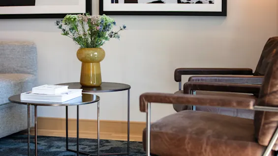 A vase with flowers on a small table and a leather chair in a cozy living room.