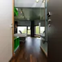 A room with two single beds, chairs, and a window view of greenery, seen through an open doorway with wooden flooring.