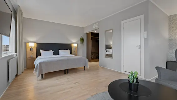 Ett ljust och inbjudande hotellrum med en bekväm säng, ljusa trägolv och en liten loungehörna.