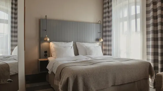 A cozy hotel room with a neatly made bed, bedside lamps, and striped curtains, ready for a comfortable stay.