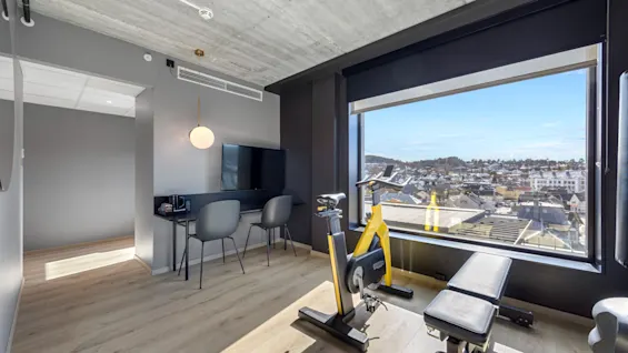 Sportssuite på Comfort Hotel Porsgrunn med trimsykkel, vektbenk og byutsikt fra et stort vindu.