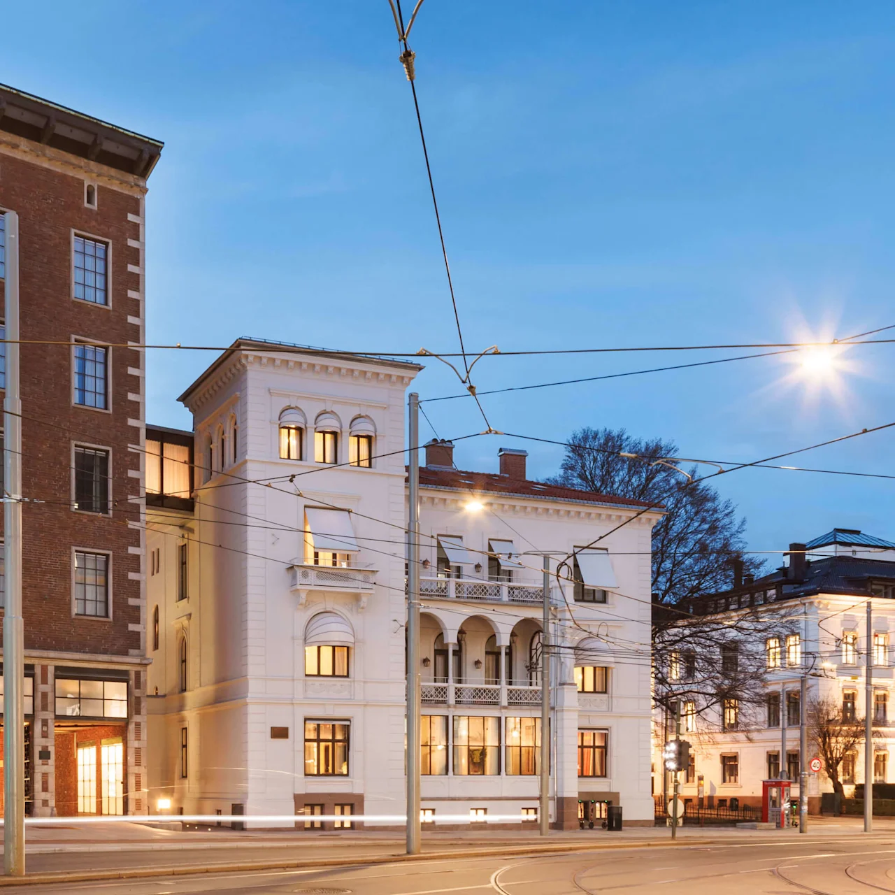 Historiske bygninger belyst i tusmørket med gadelamper og sporvognskabler, der krydser ovenfor.