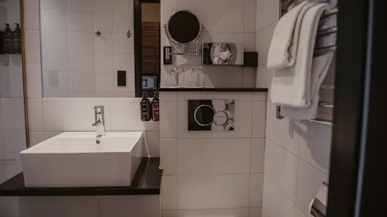 Puhdas ja moderni hotellin kylpyhuone, jossa on valkoinen pesuallas, wc, peili ja puhtaat pyyhkeet lämmitetyllä telineellä.
