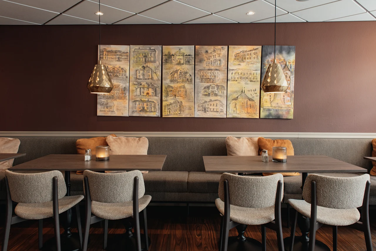 En varm och inbjudande matplats med bekväma bänkar, träbord och konstnärliga avbildningar av byggnader på väggen.