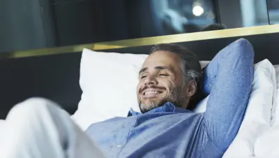 A man relaxing on a hotel bed with a smile on his face.