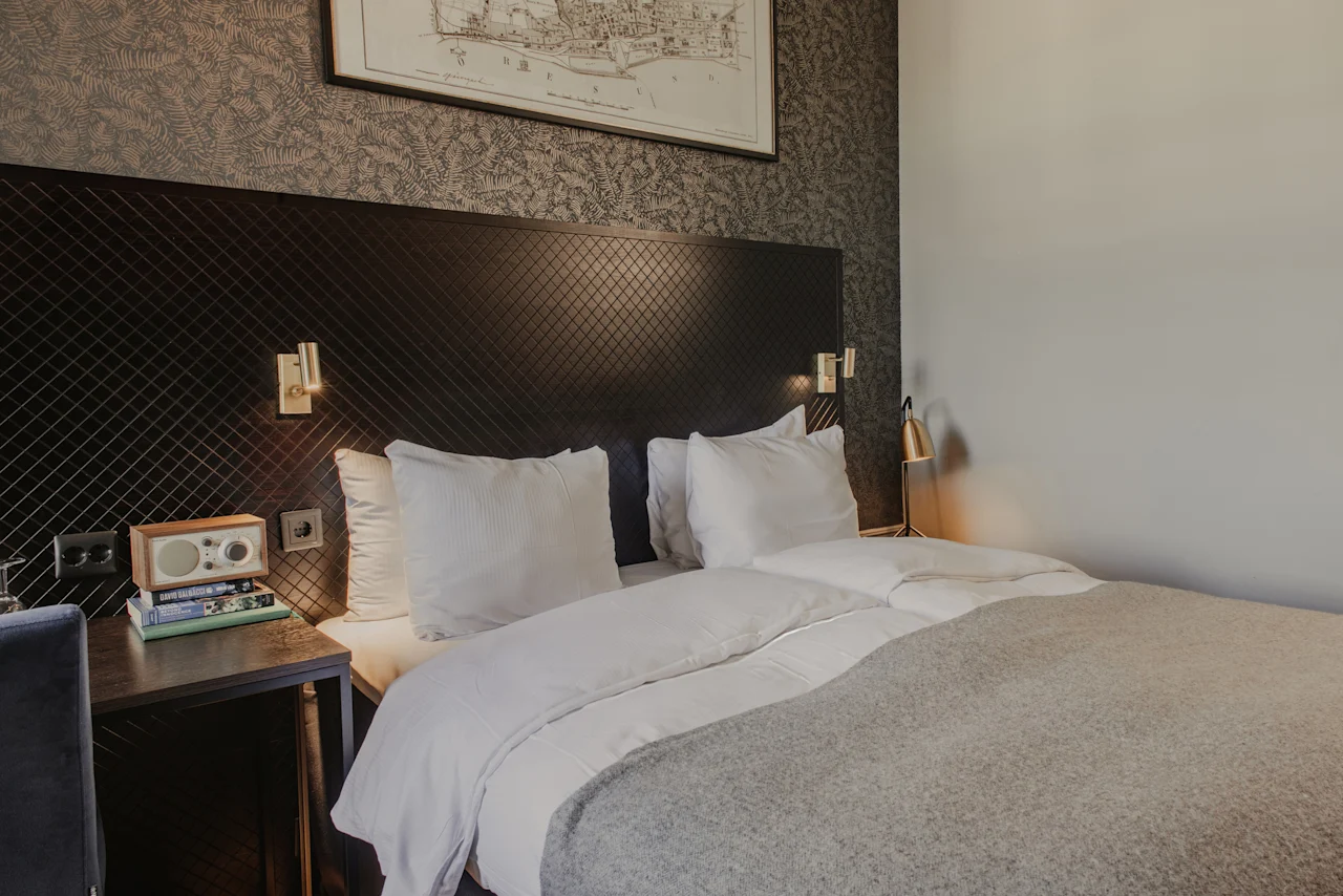 Ett bekvämt och stilfullt hotellrum på Home Hotel Grand, Helsingborg, med en säng, sängbord och dekorativ karta.