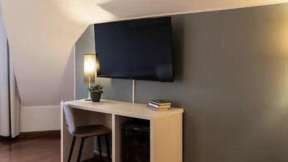 En mysig arbetsplats med en väggmonterad TV, en skrivbordslampa och ett minikylskåp, perfekt för avkoppling eller produktivitet.