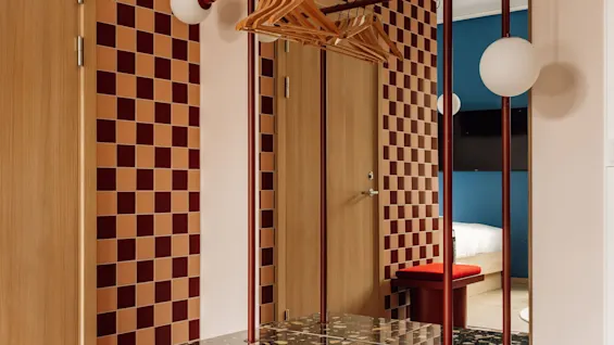 Hobo Oslo: A modern hotel room entrance with checkered tiles, a red bench, and a mirror reflecting the bedroom.