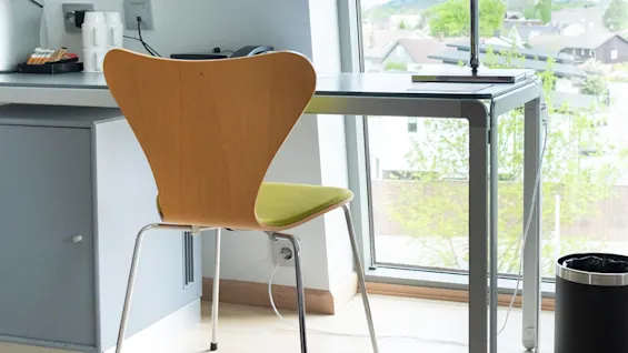 En trästol står vid ett modernt skrivbord med en hög lampa, och har utsikt över en naturskön vy genom ett stort fönster.