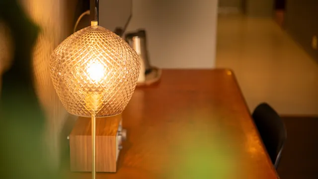 En lampe som lyser opp et trebord, kaster et varmt lys. I bakgrunnen er en vannkoker og en vegg som gir en koselig atmosfære.