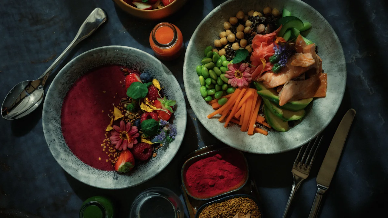 To fargerike, sunne matskåler, en smoothiebowl med bær og blomster, den andre en mettende skål med grønnsaker og fisk.