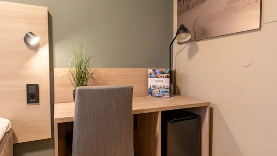 En godt opplyst hotellromsarbeidsplass med et treskrivebord, stol og en brosjyre for TROMSO, perfekt for å planlegge eventyr.