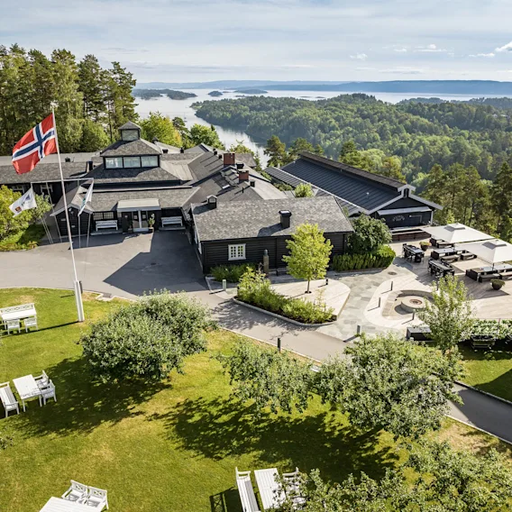 Flyfoto av et vakkert trehotell med utsikt over en naturskjønn fjord med øyer i Norge.