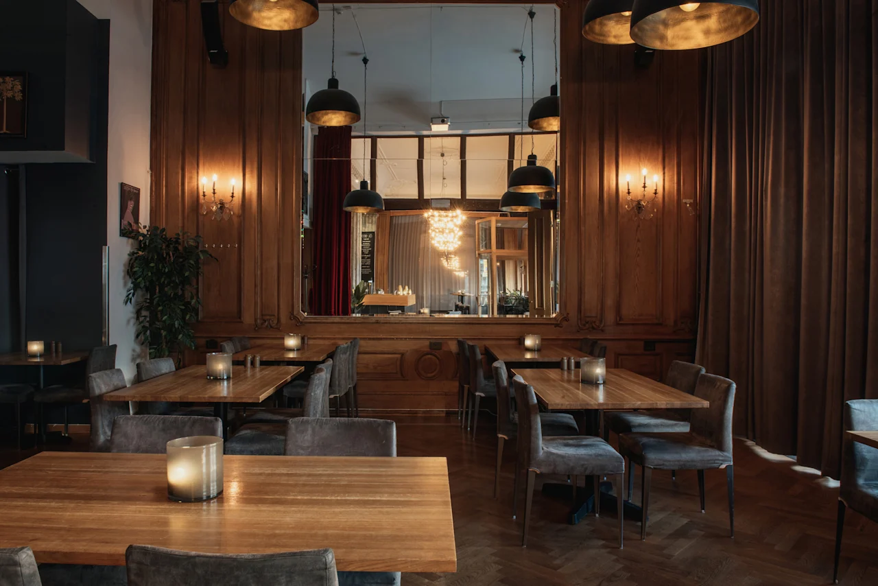 En mysig matplats på Home Hotel Grand, Helsingborg, med träbord, bekväma stolar och varm belysning från levande ljus och taklampor.