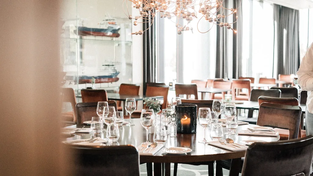 En restaurant spisesal med dekkede bord, stoler, et tent lys og dekorative skipsmodeller.