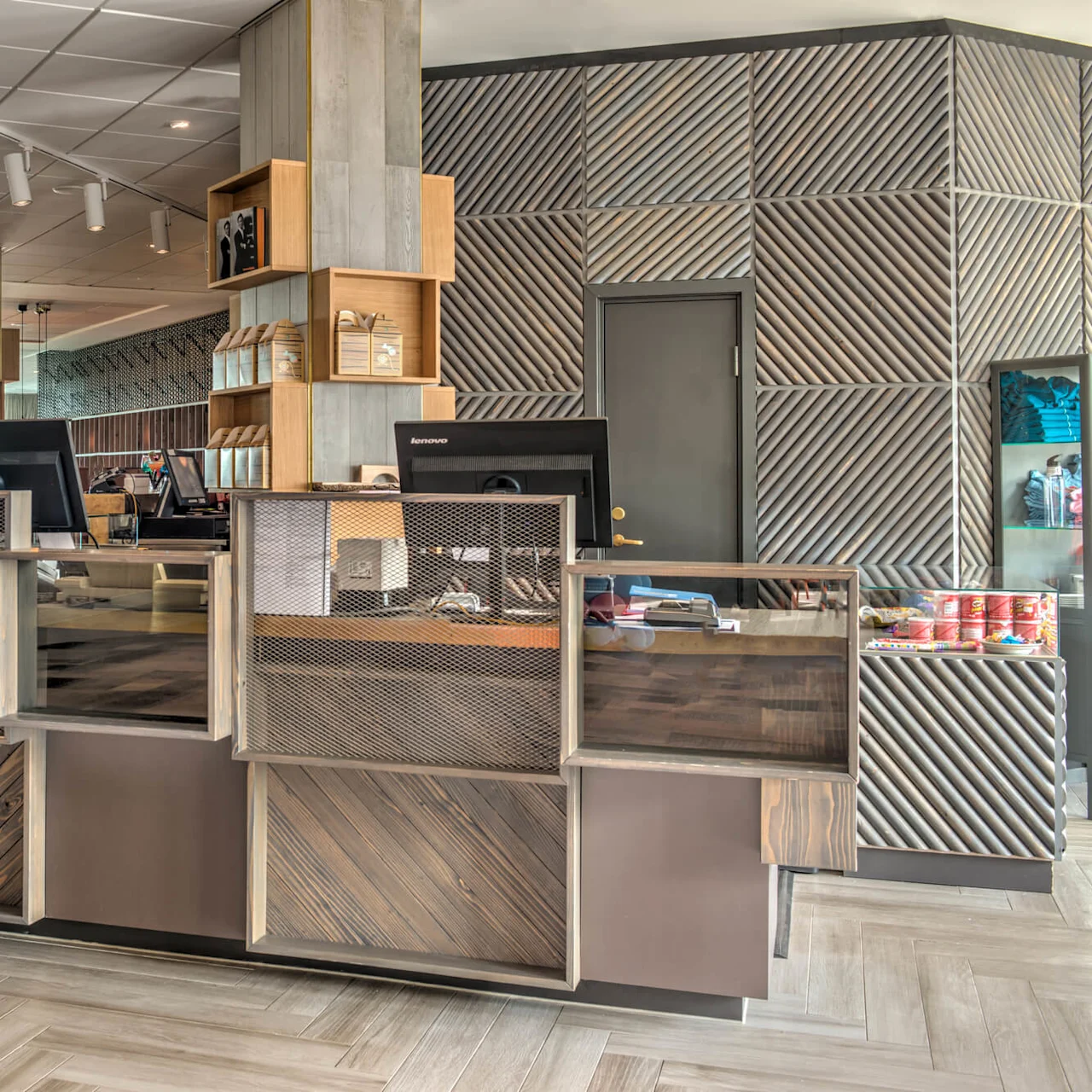 A modern reception desk featuring computer monitors and decorative wood paneling, situated in a stylish lobby with contemporary furnishings and ambient lighting.