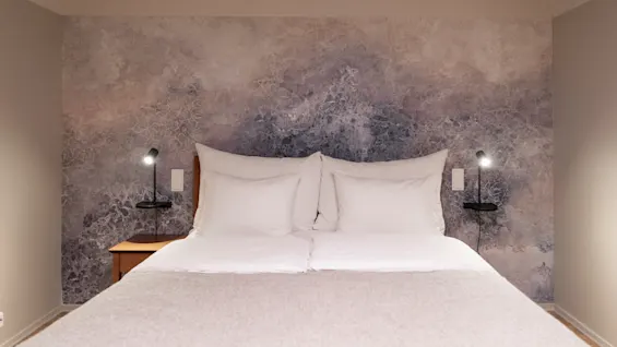 A cozy bedroom with a large bed, white bedding, and a textured accent wall. Two bedside lamps provide soft lighting.