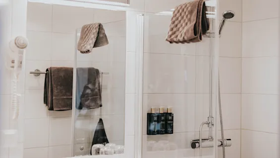 Et moderne badeværelse med glasbrusekabine, hængende håndklæder og toiletartikler.