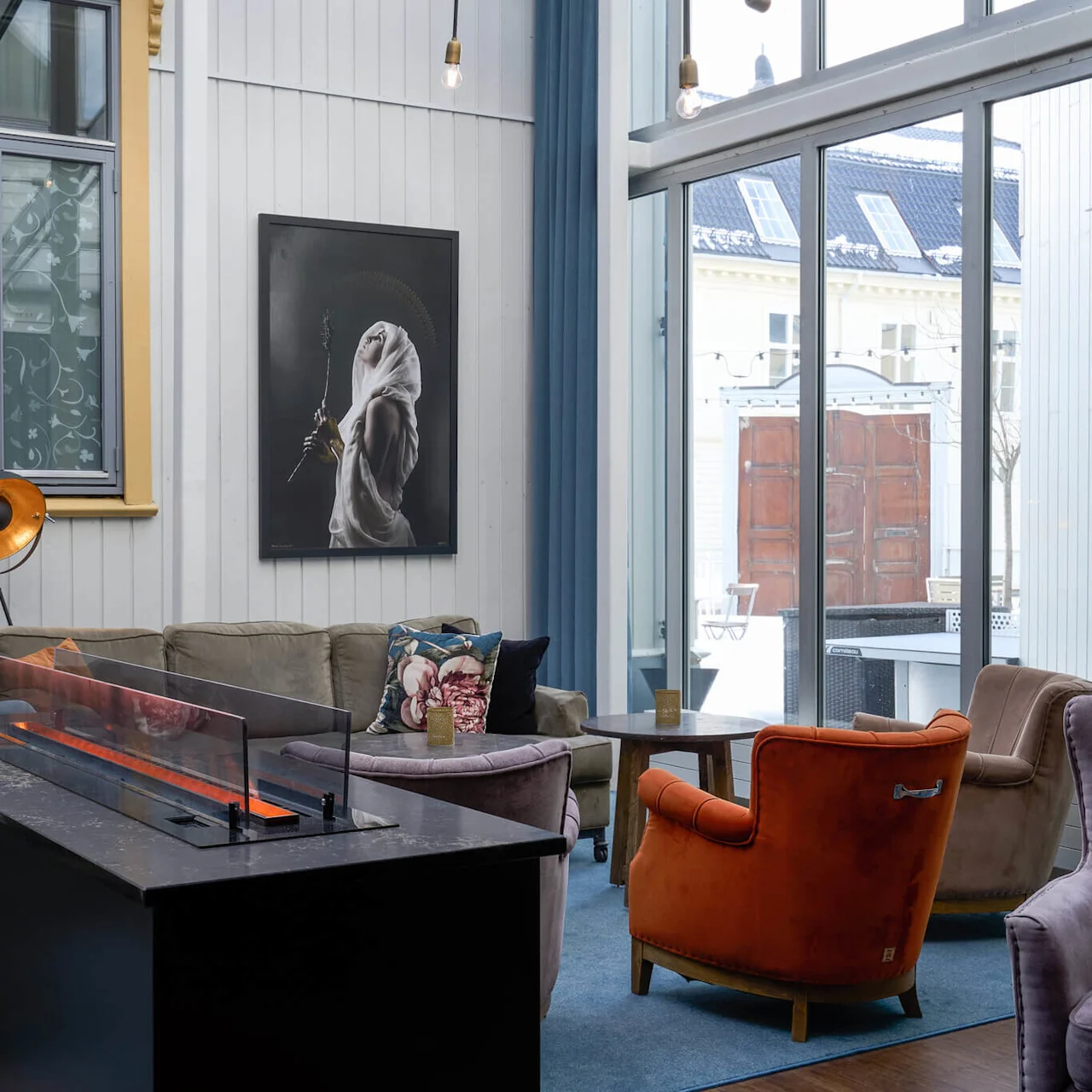 En hyggelig lounge med sofaer, moderne pejs, og kunst i et rum med store vinduer og blød belysning.